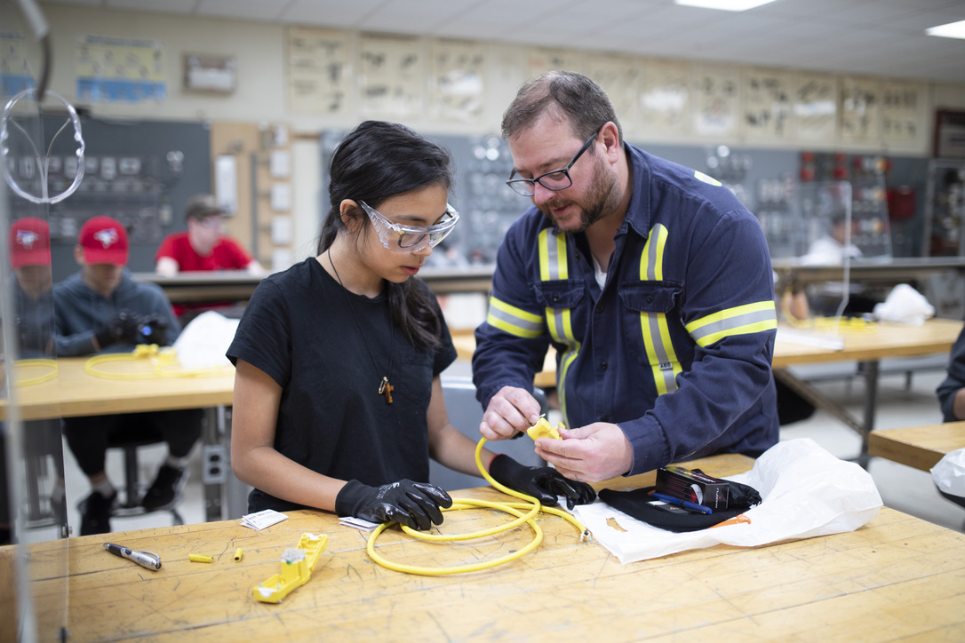 Volunteer instructor guiding a summer-camp student through extension-cord assembly