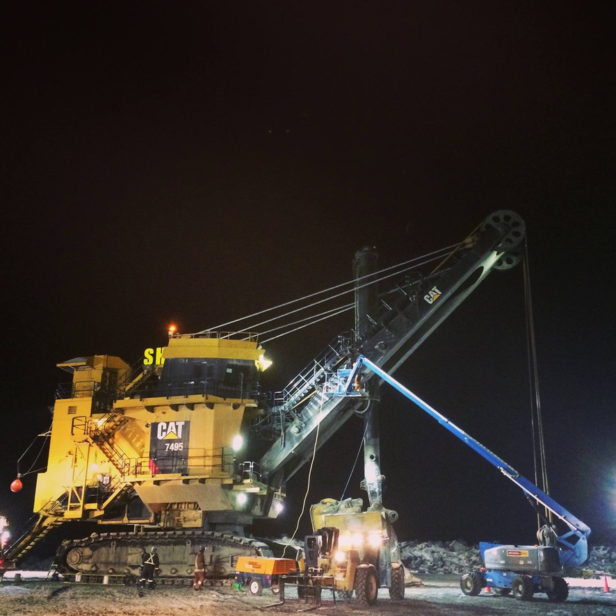 Large mining shovel at night with maintenance equipment alongside it