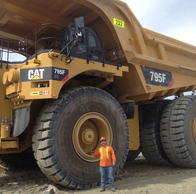 Shawn beside the enormous front tire of a CAT 795F mining haul truck