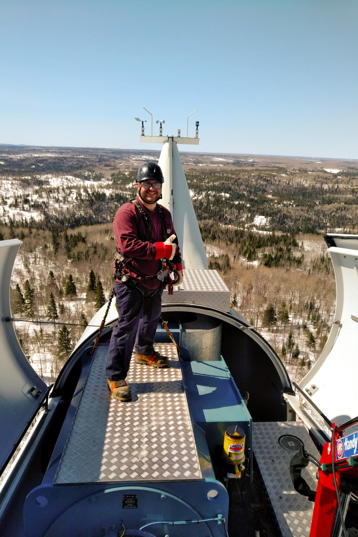 Shawn on a wind turbine above a forested landscape during renewable-energy work